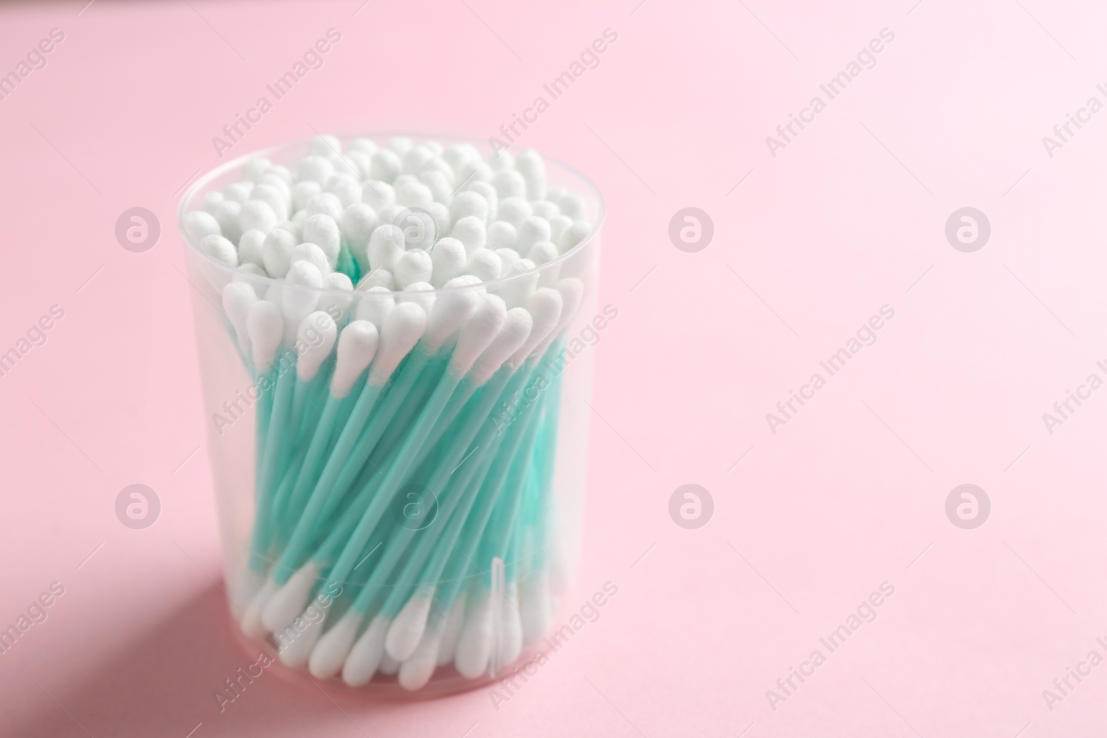 Photo of Plastic container with cotton swabs on color background. Space for text