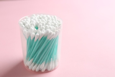 Photo of Plastic container with cotton swabs on color background. Space for text