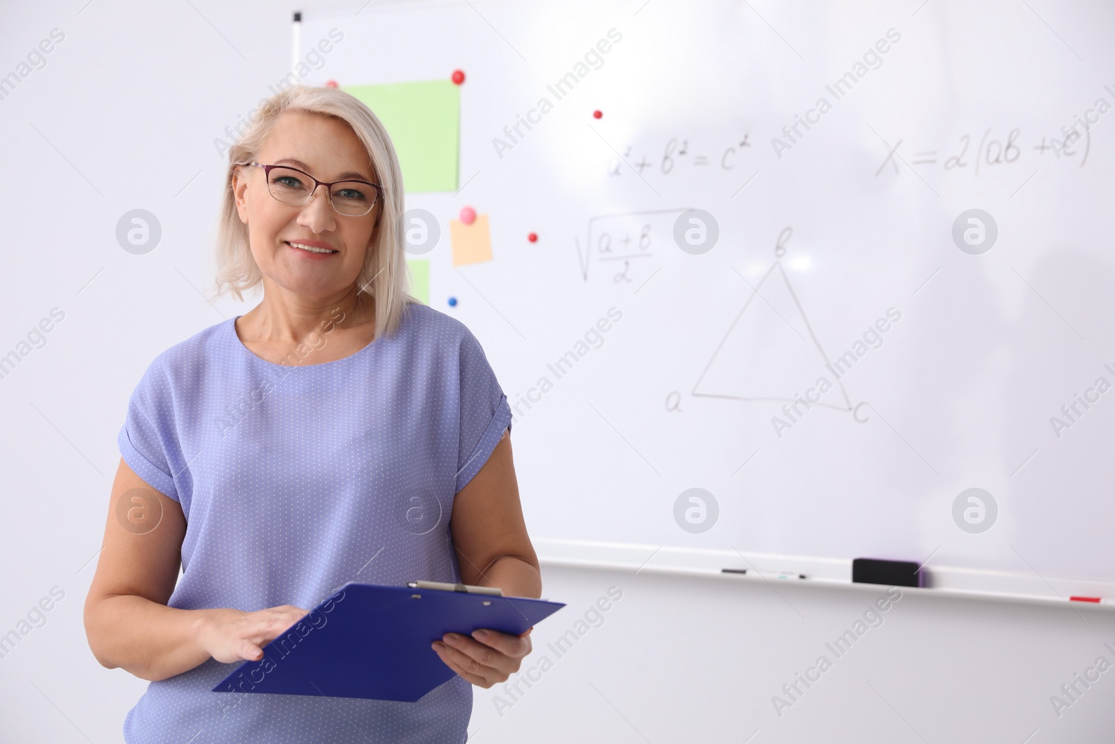 Photo of Mature teacher with clipboard near whiteboard in modern classroom. Space for text