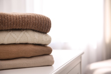 Stack of folded warm sweaters on white table indoors, closeup. Space for text