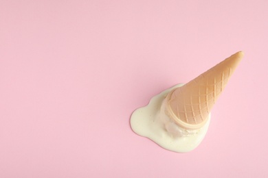 Melted vanilla ice cream in wafer cone on pink background, above view. Space for text