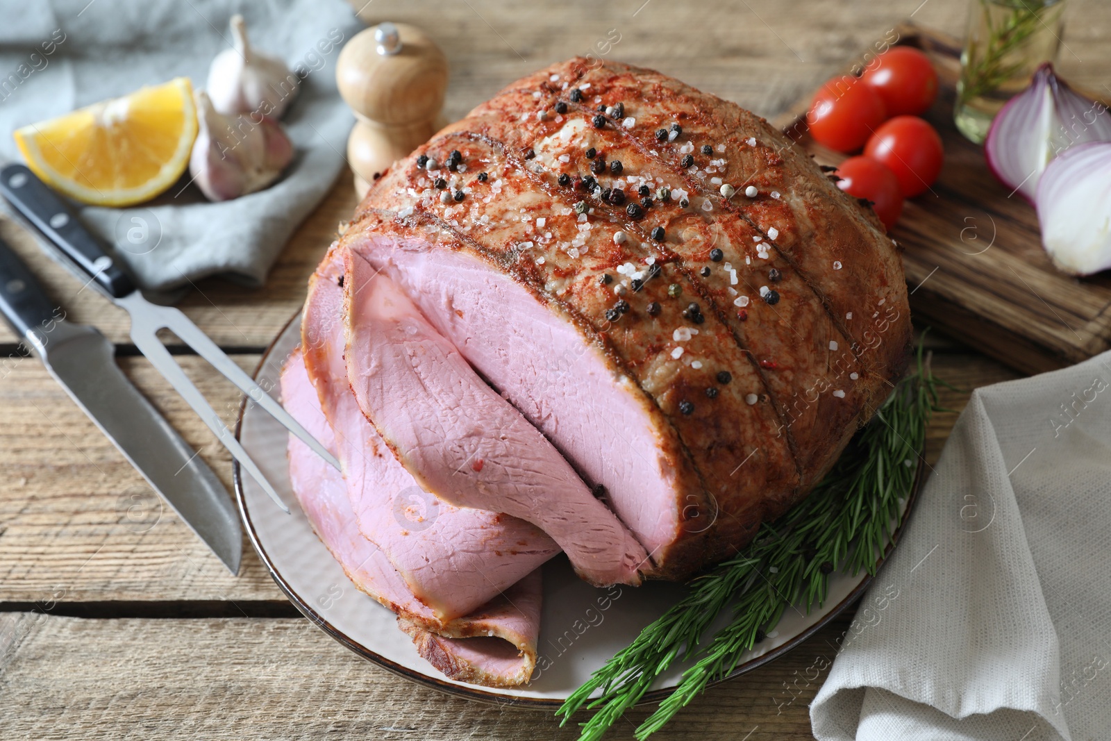 Photo of Delicious baked ham, carving fork, knife and rosemary on wooden table, closeup