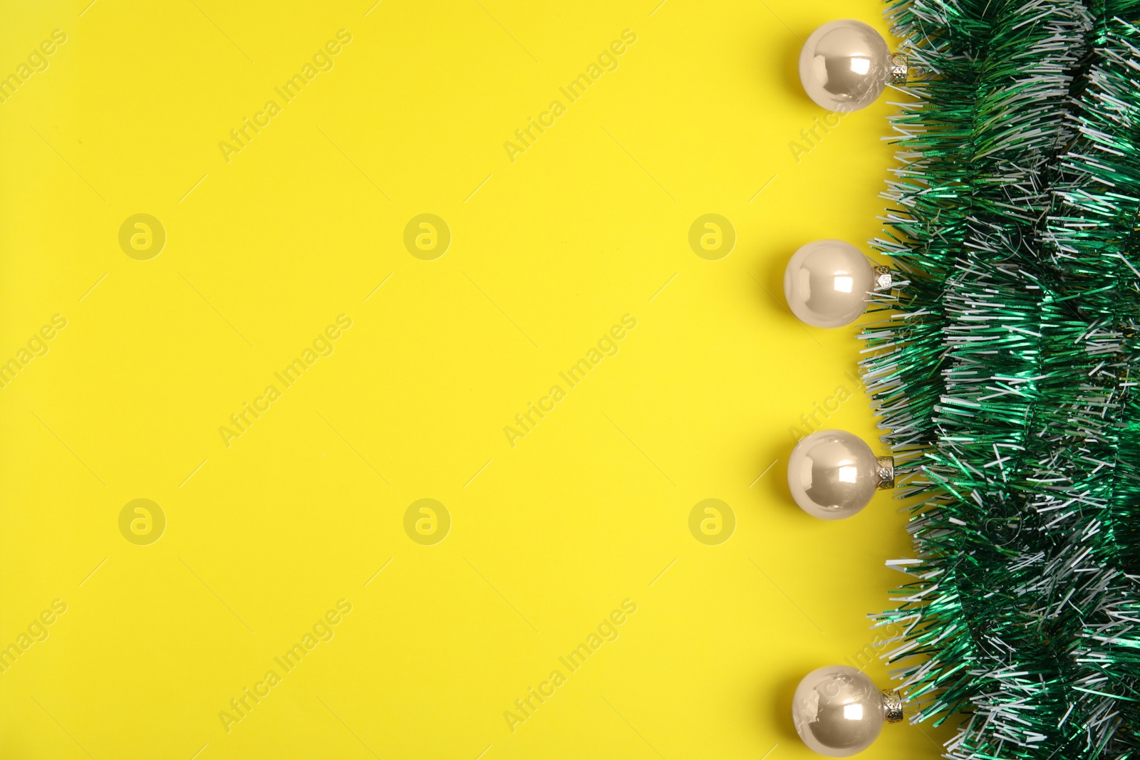 Photo of Green tinsel and Christmas balls on yellow background, flat lay. Space for text