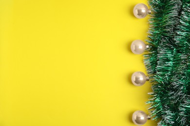 Photo of Green tinsel and Christmas balls on yellow background, flat lay. Space for text