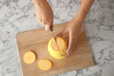 Photo of Woman cutting ripe spaghetti squash on marble table, top view