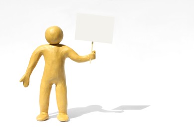 Photo of Human figure made of yellow plasticine holding blank sign on white background. Space for text