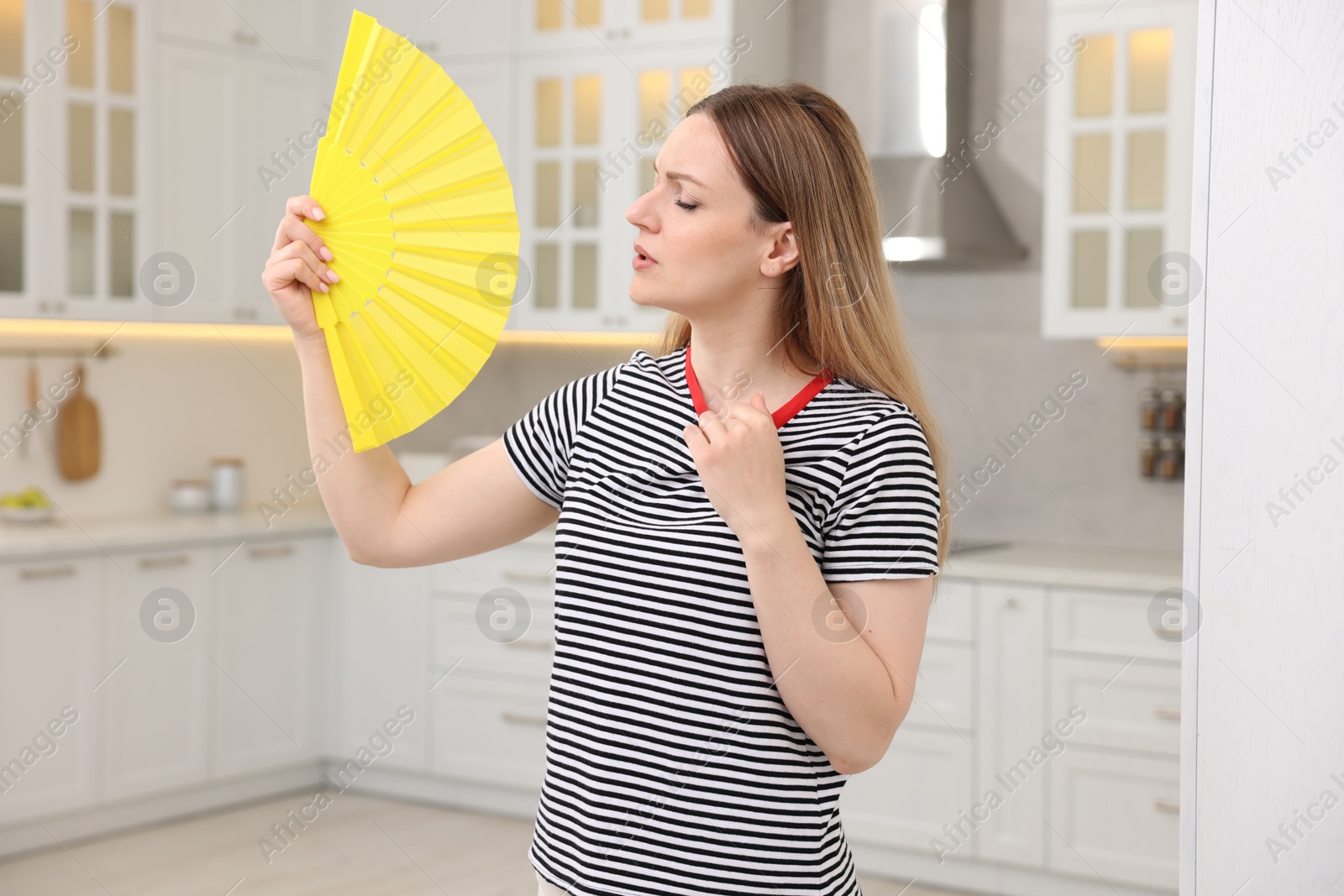 Photo of Woman waving yellow hand fan to cool herself in kitchen