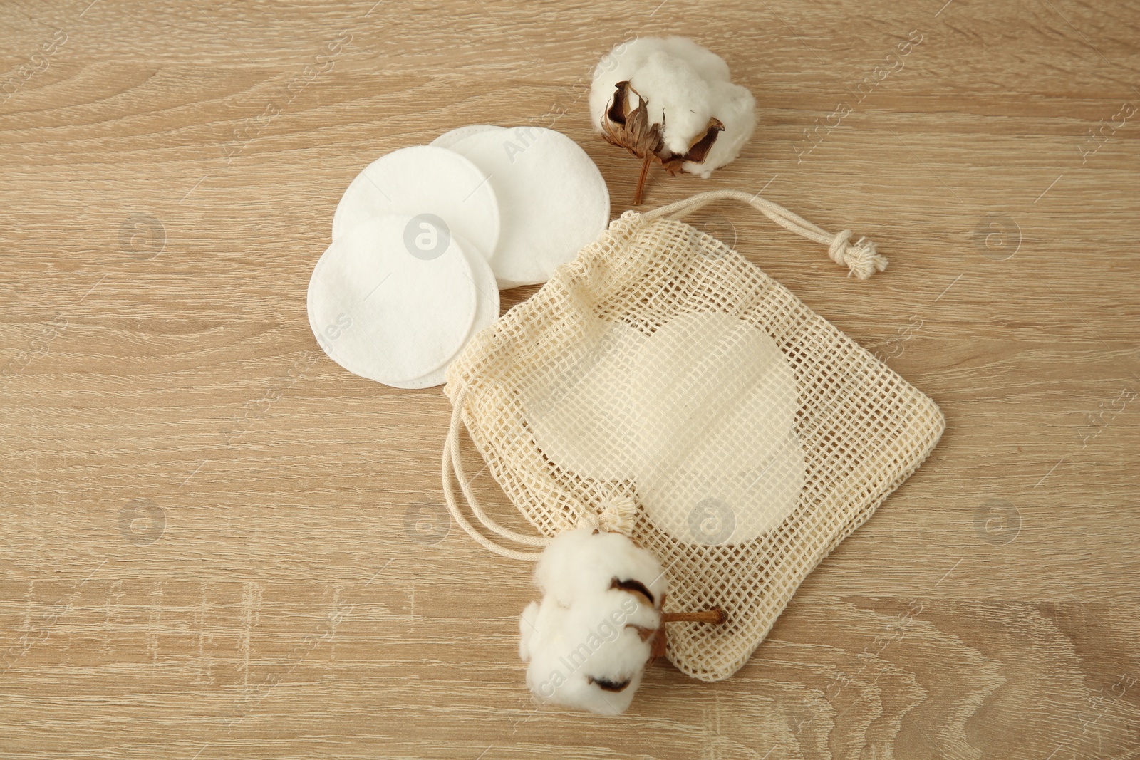 Photo of Cotton pads, bag and flowers on wooden table, above view. Space for text