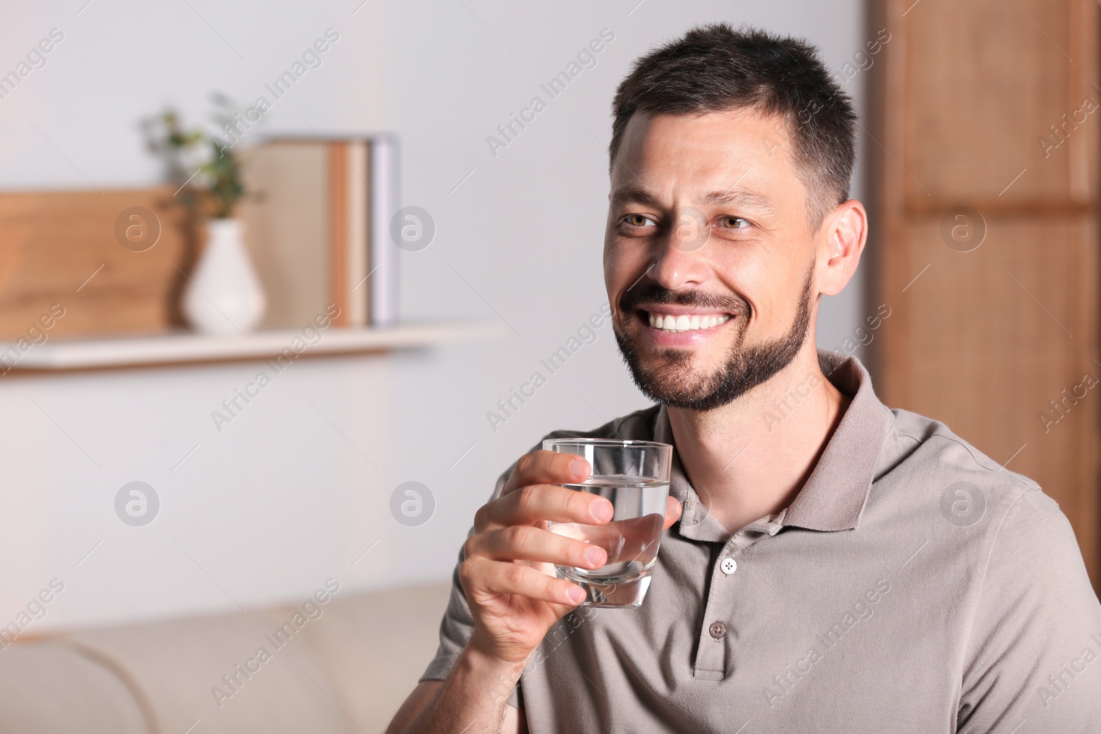 Photo of Happy man with glass of water indoors. Refreshing drink