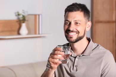Happy man with glass of water indoors. Refreshing drink