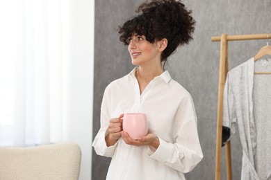 Photo of Beautiful young woman in stylish pyjama with cup of drink at home