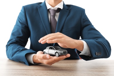 Photo of Insurance agent holding toy car in hands over table against white background