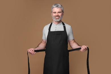 Photo of Happy man wearing kitchen apron on brown background. Mockup for design