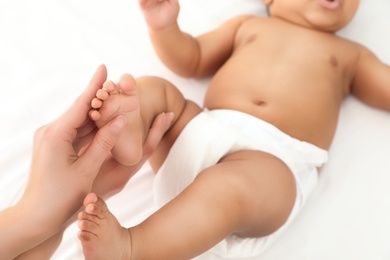 Mother and her cute child on white bed, closeup. Baby massage and exercises