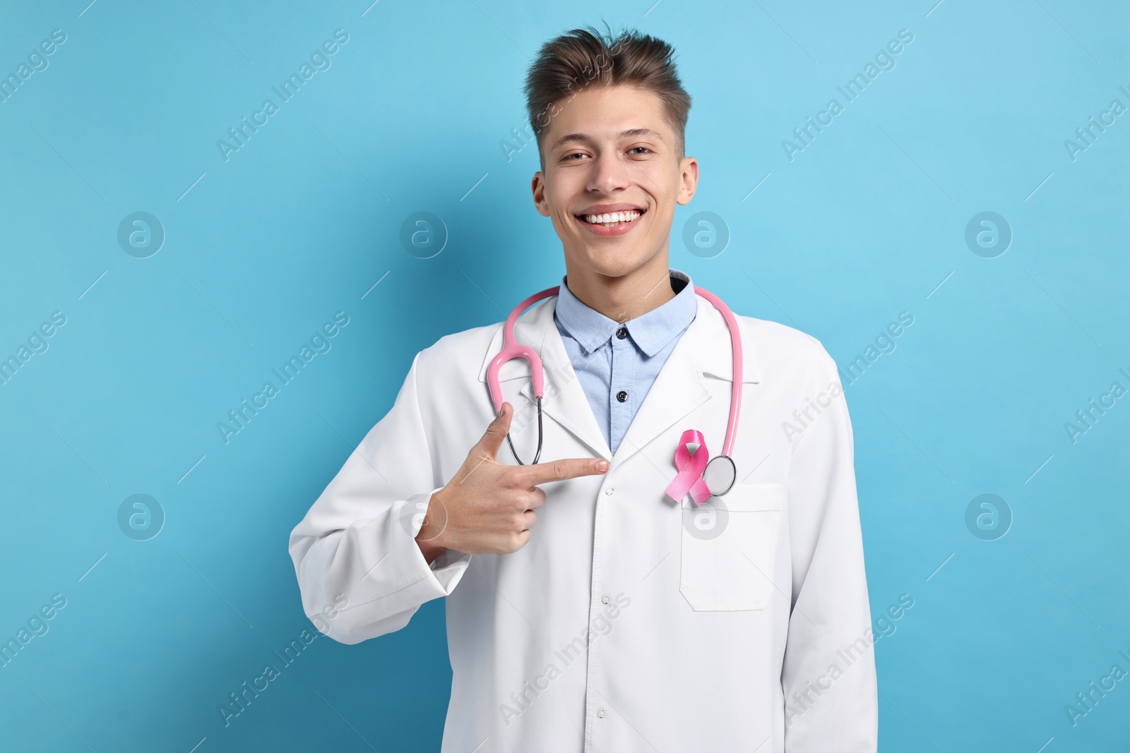 Photo of Mammologist pointing at pink ribbon on light blue background. Breast cancer awareness