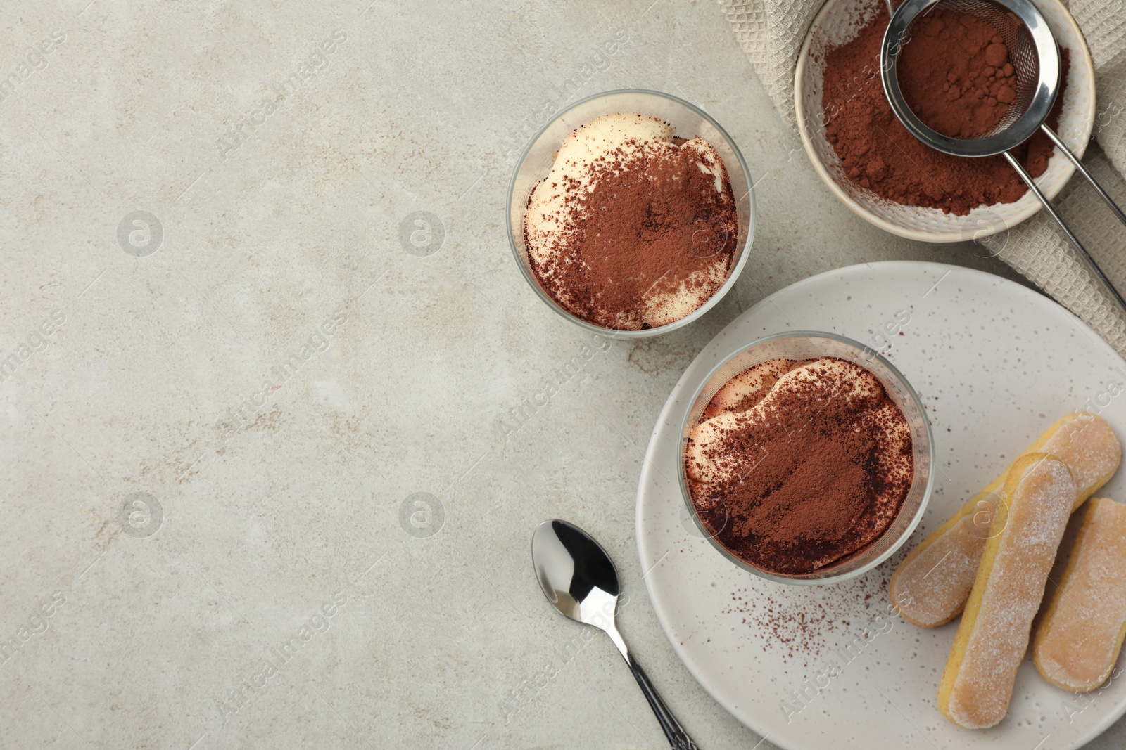 Photo of Delicious tiramisu in glasses, cookies and sieve with cocoa powder on light table, flat lay. Space for text