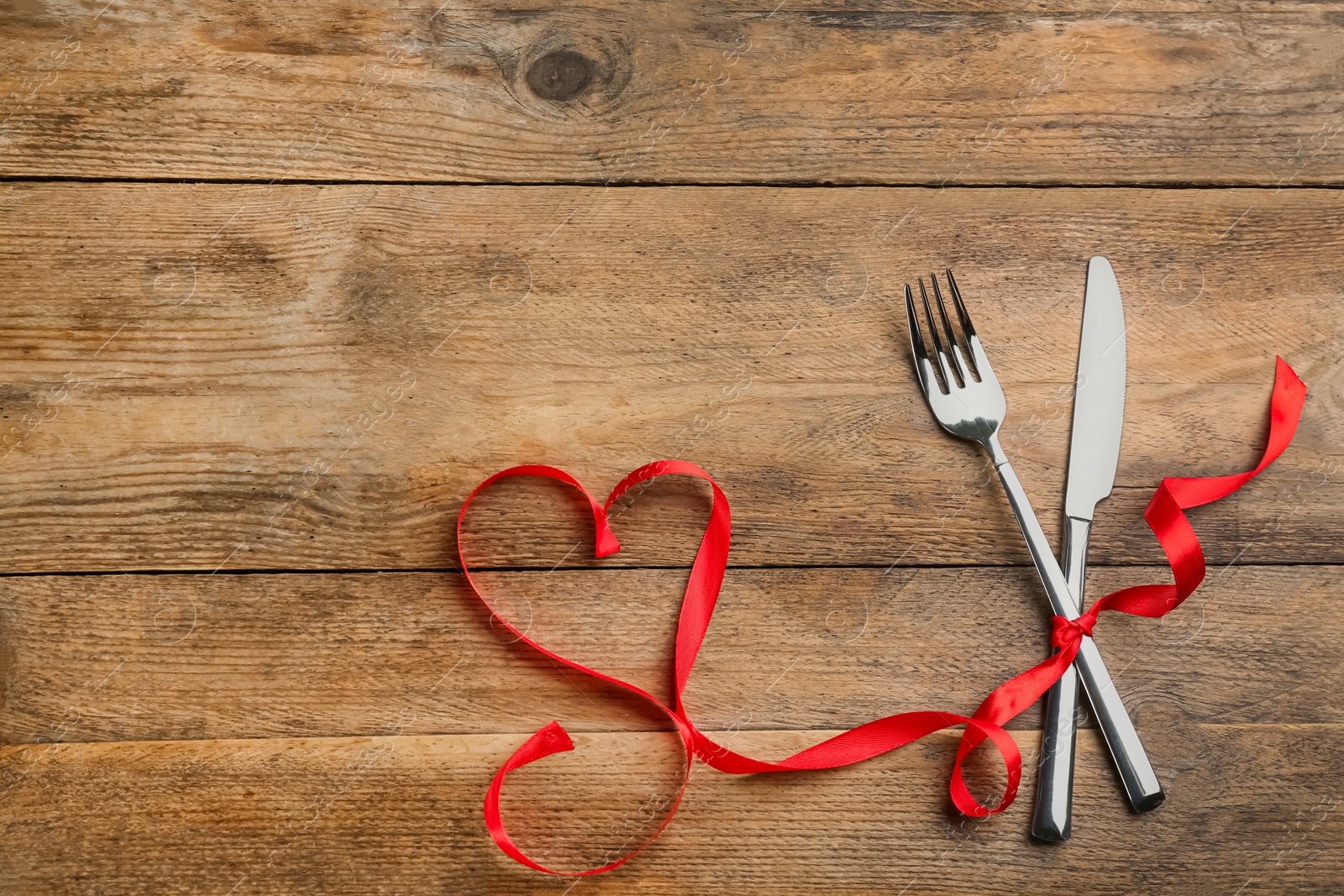 Photo of Cutlery set and red ribbon on wooden background, flat lay with space for text. Valentine's Day dinner