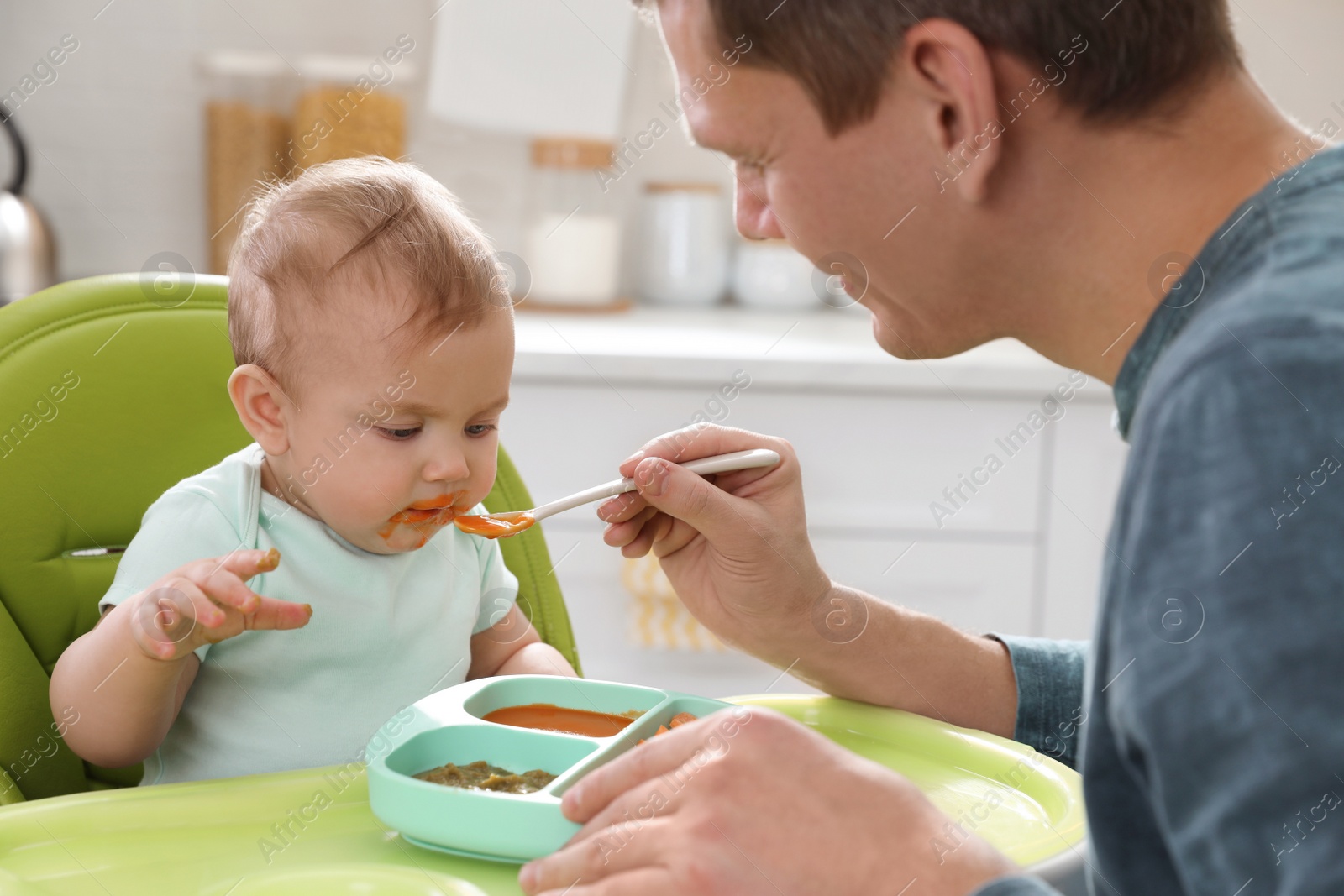 Photo of Father feeding his cute little baby in kitchen