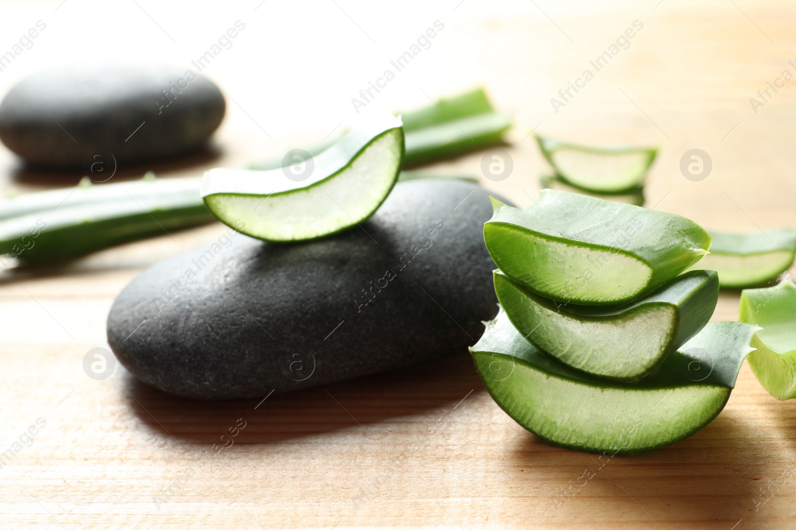 Photo of Fresh sliced aloe vera leaves and spa stones on wooden table