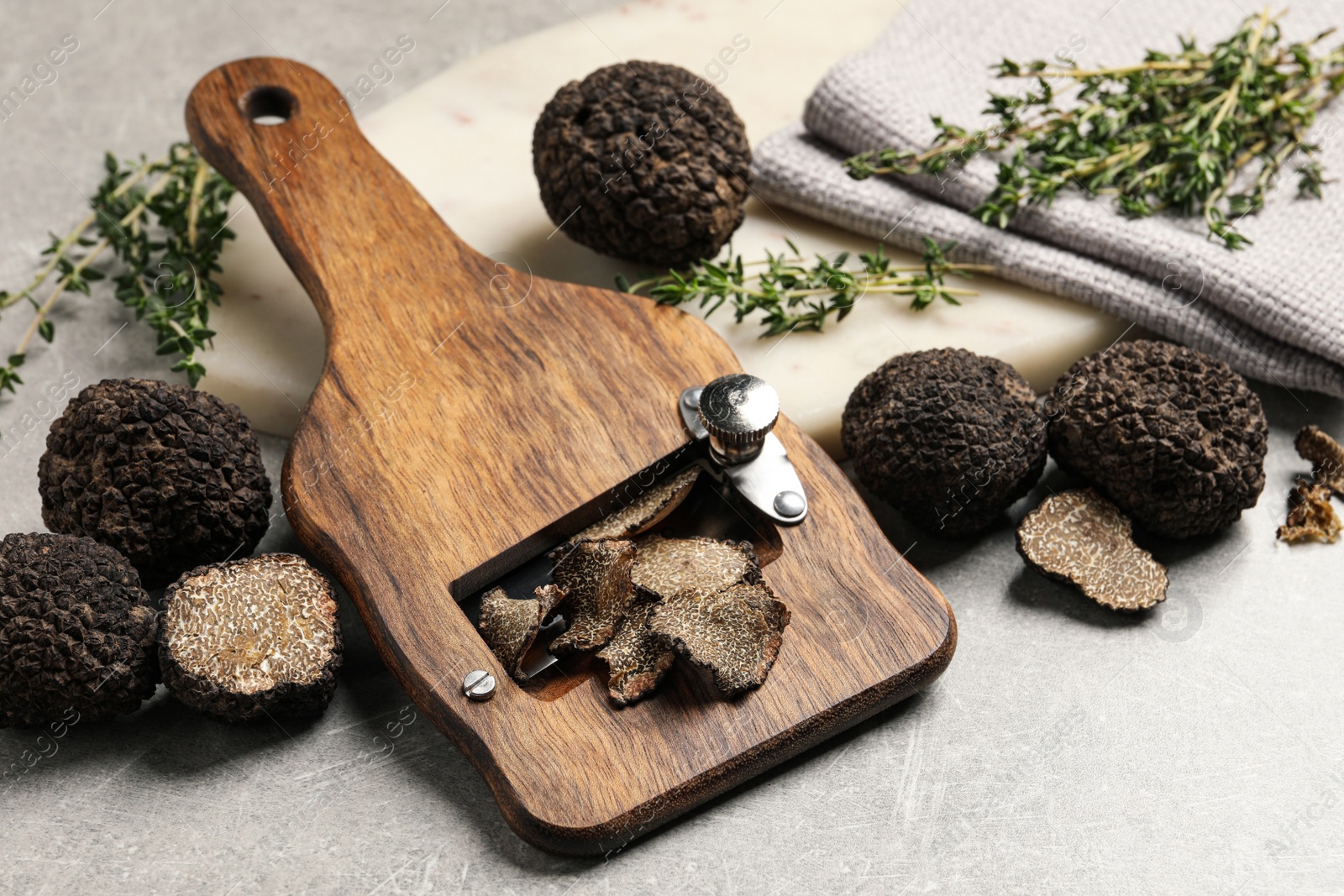 Photo of Fresh black truffles, slicer and thyme on grey table