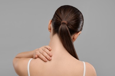 Woman touching her neck on grey background, back view