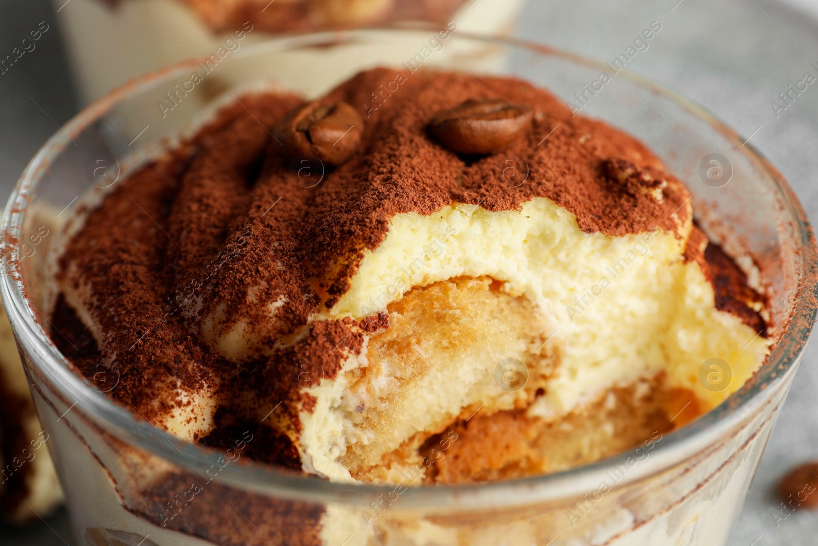 Photo of Delicious tiramisu in glass and coffee beans on table, closeup