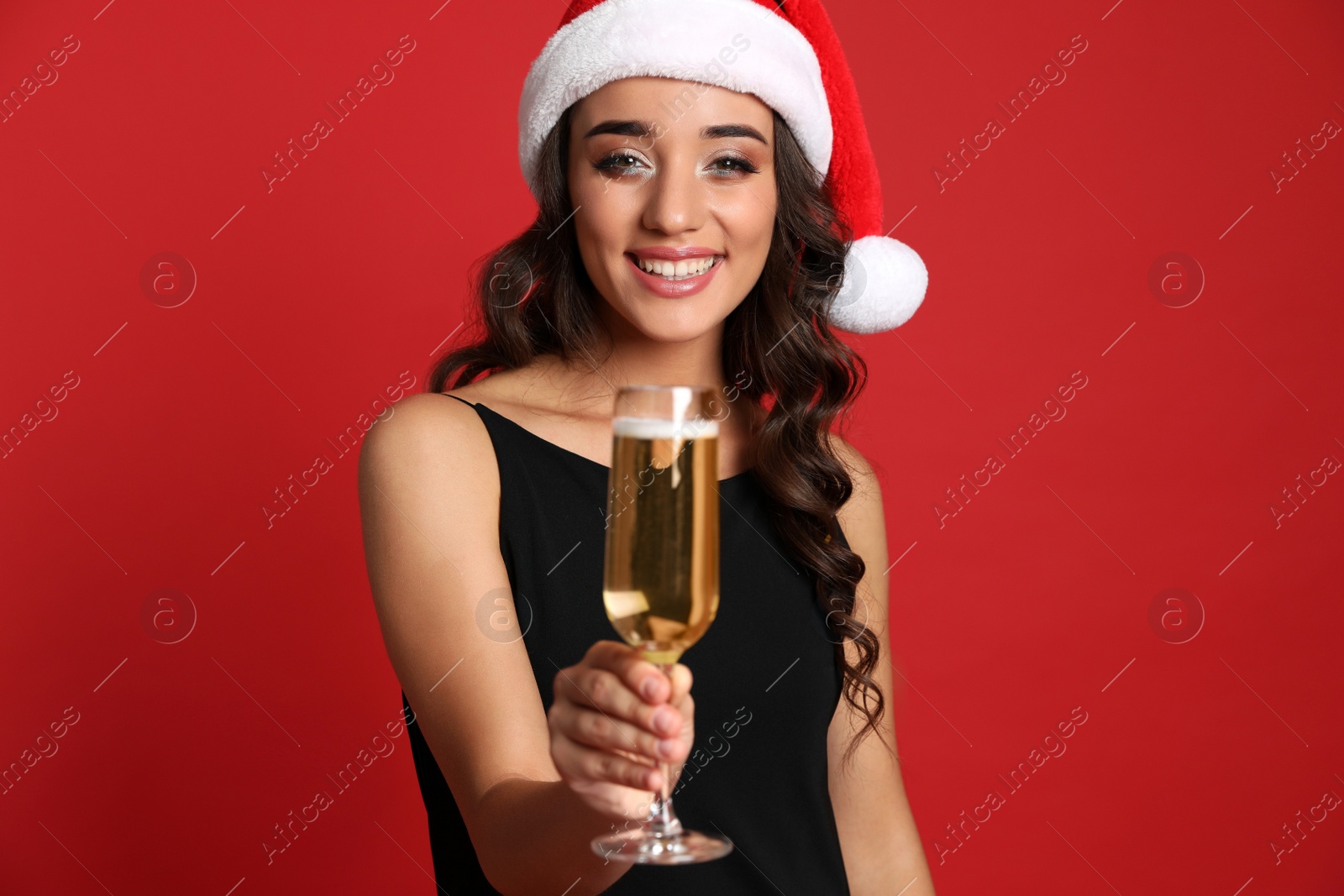 Photo of Beautiful woman in Santa hat holding glass of champagne on red background. Christmas party