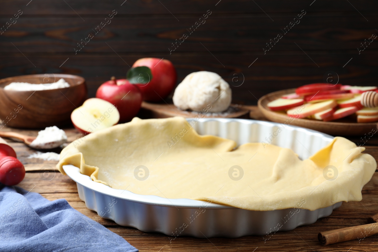 Photo of Baking dish with raw dough for apple pie and ingredients on wooden table