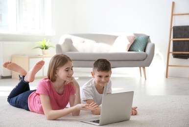Photo of Teenage girl and her brother with laptop lying on cozy carpet at home