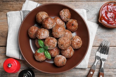Tasty cooked meatballs with basil served on wooden table, flat lay
