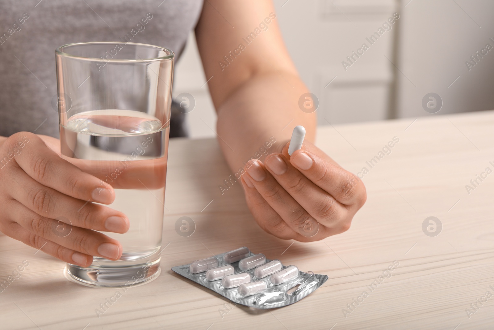 Photo of Woman with pill and glass of water at white wooden table, closeup. Space for text