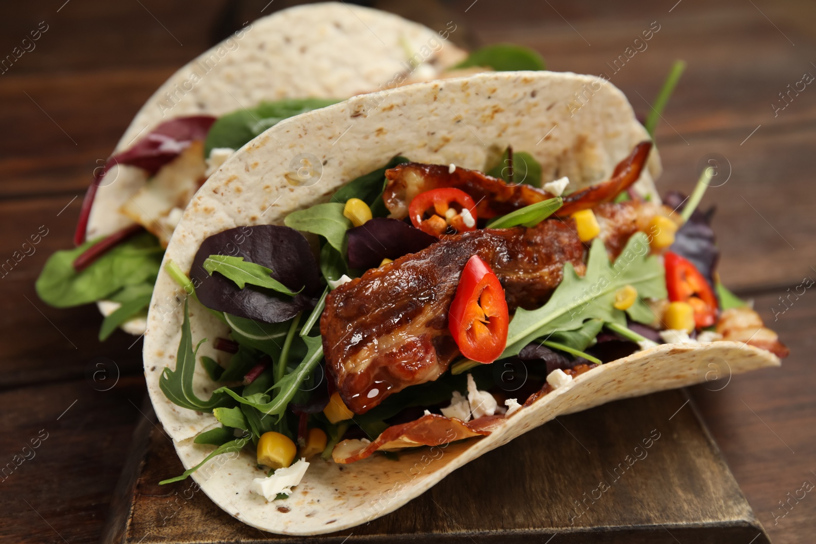 Photo of Delicious tacos with fried bacon, vegetables and cheese on wooden board, closeup