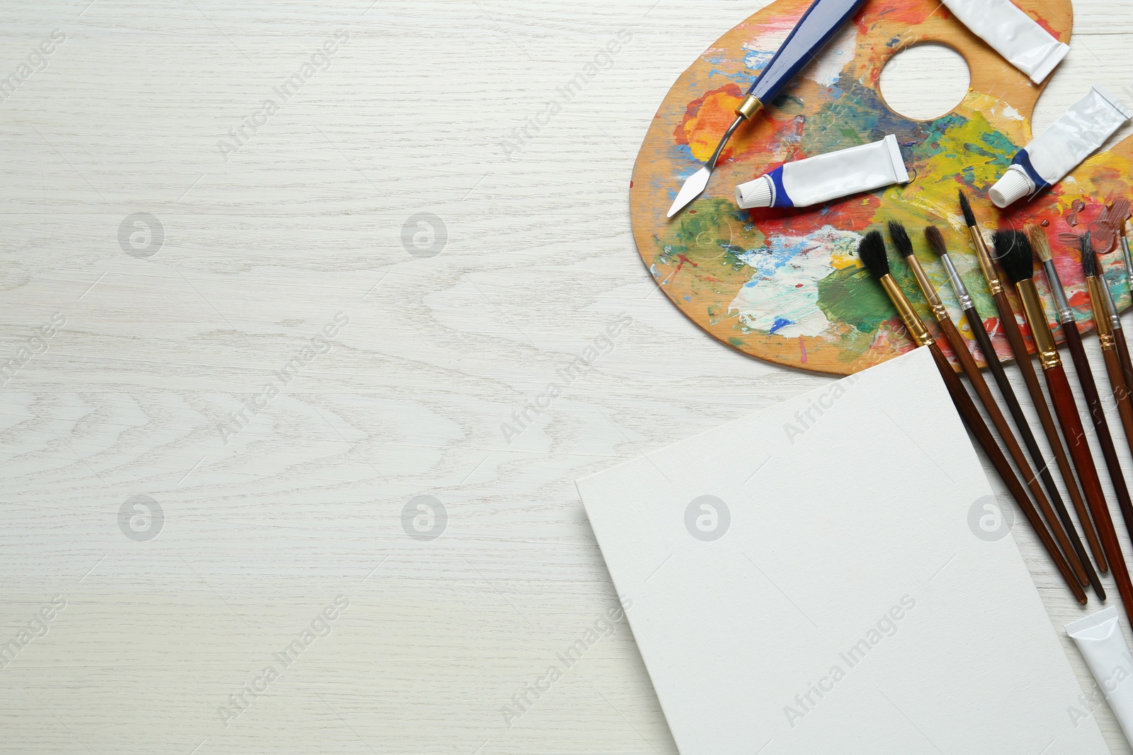 Photo of Blank canvas, tools, palette and paints on white wooden table, flat lay. Space for text