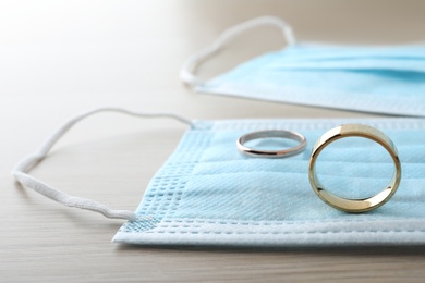 Photo of Protective masks and wedding rings on wooden table. Divorce during coronavirus quarantine