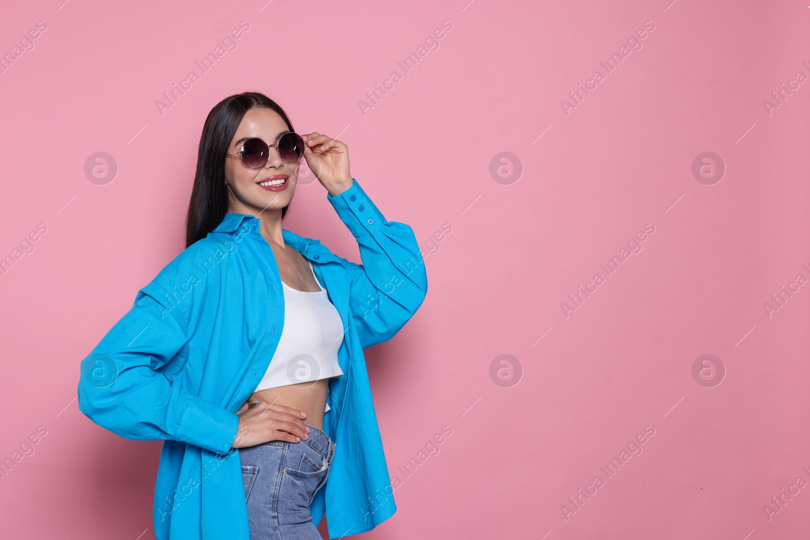 Photo of Attractive happy woman touching fashionable sunglasses against pink background. Space for text