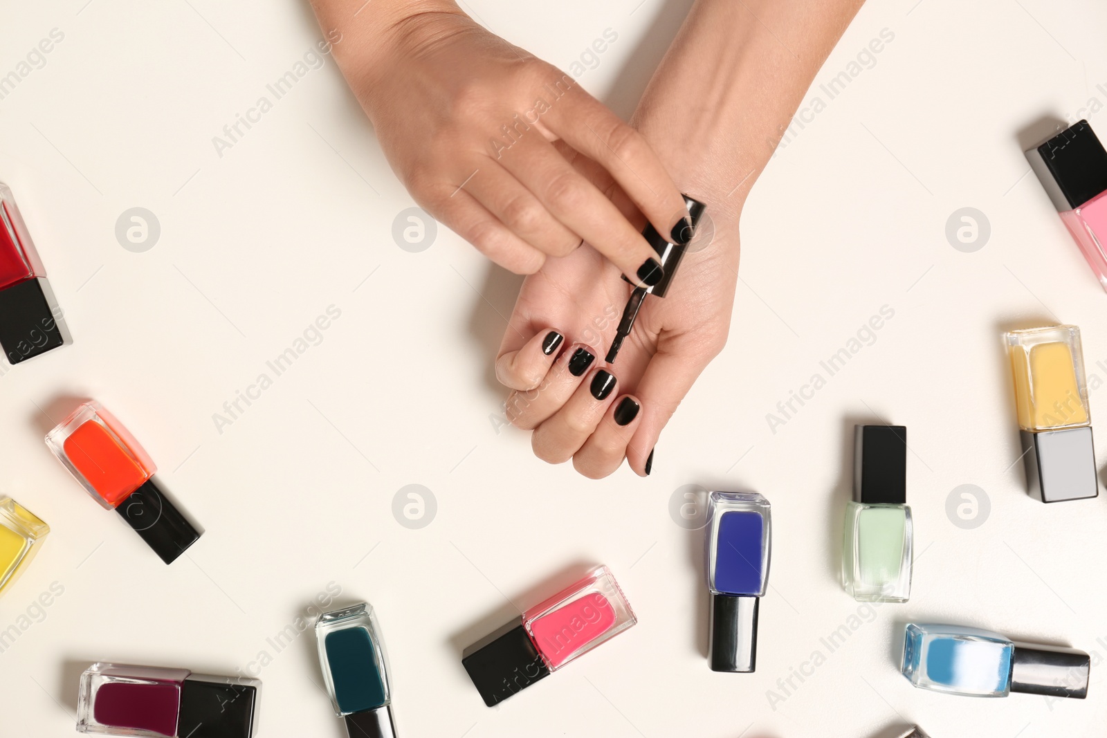 Photo of Woman applying nail polish near bottles on white background, top view