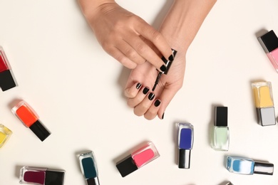 Woman applying nail polish near bottles on white background, top view