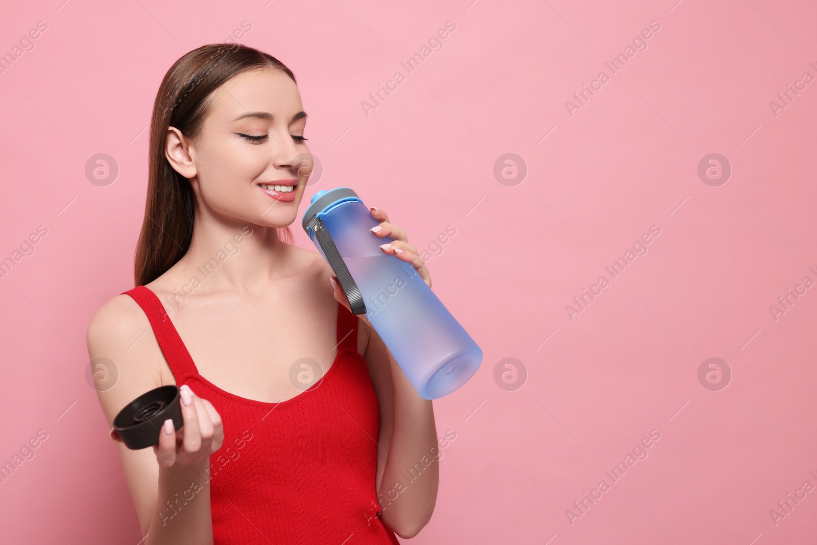 Photo of Beautiful young woman with transparent bottle on pink background, space for text