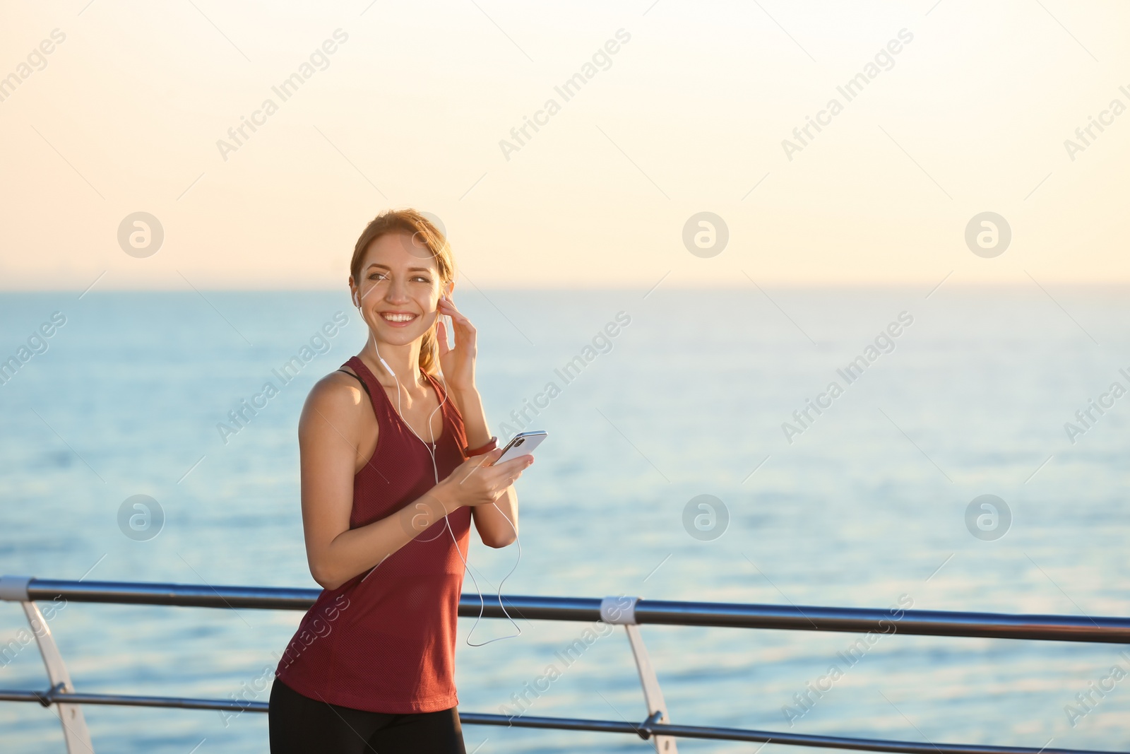 Photo of Young woman choosing music for fitness exercises on pier in morning