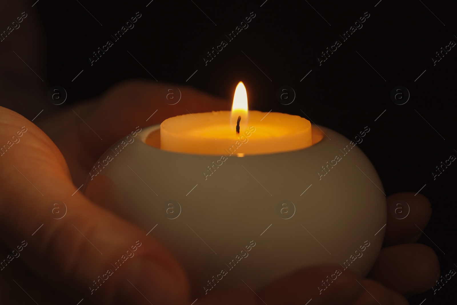 Photo of Young person holding burning candle in darkness, closeup