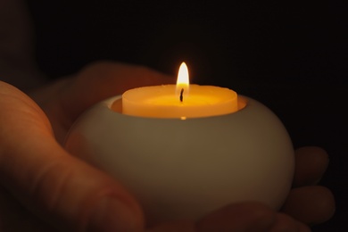 Photo of Young person holding burning candle in darkness, closeup