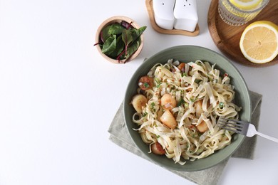 Delicious scallop pasta with spices in bowl served on white table, flat lay. Space for text