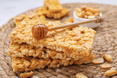 Photo of Delicious peanut bars (kozinaki) and dipper with honey on wicker mat, closeup