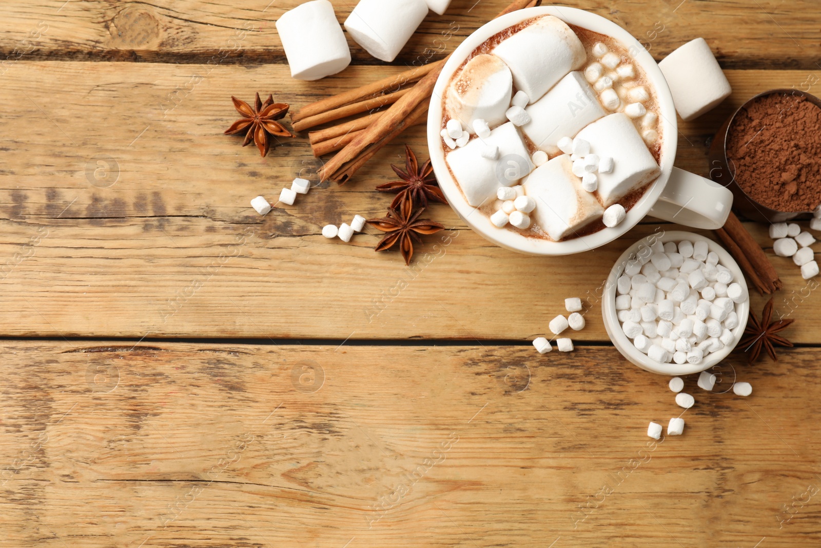 Photo of Tasty hot chocolate with marshmallows and ingredients on wooden table, flat lay. Space for text