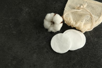 Photo of Cotton pads, bag and flower on black table, above view. Space for text