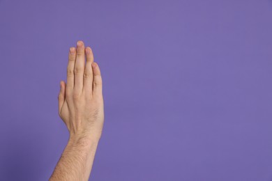 Man giving high five on purple background, closeup of hand. Space for text