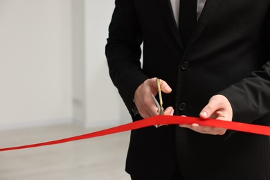 Photo of Man cutting red ribbon with scissors indoors, closeup. Space for text