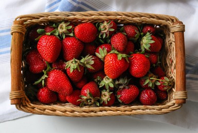 Photo of Wicker basket with ripe strawberries and napkin on white table, top view