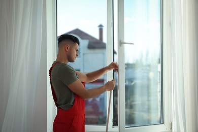 Worker putting rubber draught strip onto window indoors