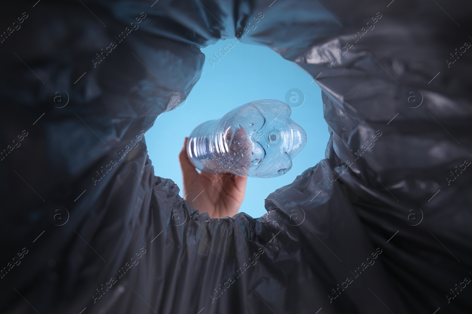 Photo of Bottom view of woman throwing plastic bottle into trash bin on light blue background, closeup